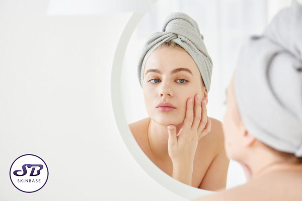 a woman with her hair wrapped up in a towel examining her skin in the mirror